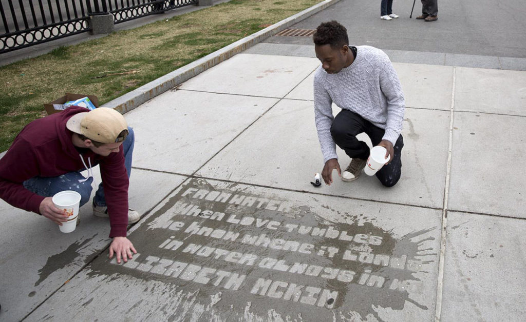 Mayor's Mural Crew staff Connor Woods and Jerome Jones pour water onto a sidewalk near Park St. station to see where poems will appear when it rains. (Robin Lubbock/WBUR)