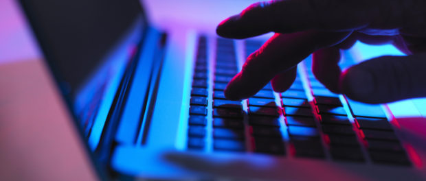 Silhouette of male hand typing on laptop keyboard at night