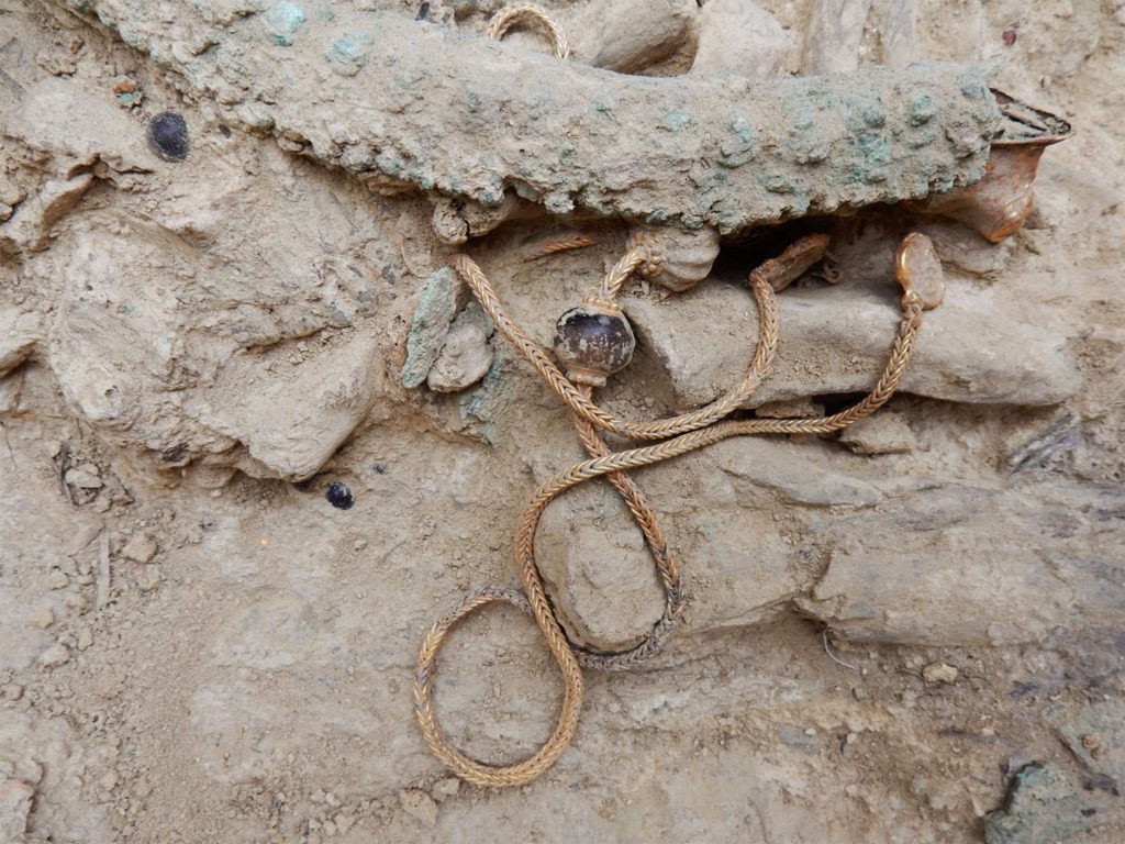 This picture provided by Greece's Culture Ministry on Monday, Oct. 26, 2015, shows a long gold chain, decorated with semi-precious stones and hammered-gold plant decorations, as it was found in a 3,500-year-old warrior's tomb. Authorities say a 3,500-year-old, treasure-filled grave of a warrior has been discovered near an ancient palace in southern Greece. The Culture Ministry says the grave is the most spectacular discovery of its kind from the Mycenaean era in more than six decades. It contained about 1,400 artefacts, including gold and silver jewelry, cups, bronze vases, engraved gemstones and an ornate ivory-and gilt-hilted sword. (Greek Culture Ministry via AP)