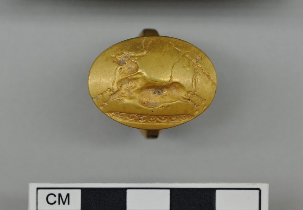 This picture provided by Greece's Culture Ministry on Monday, Oct. 26, 2015, shows a gold signet ring decorated with two acrobats vaulting over a bull, found in a 3,500-year-old warrior's tomb. Authorities say a 3,500-year-old, treasure-filled grave of a warrior has been discovered near an ancient palace in southern Greece. The Culture Ministry says the grave is the most spectacular discovery of its kind from the Mycenaean era in more than six decades. It contained about 1,400 artefacts, including gold and silver jewelry, cups, bronze vases, engraved gemstones and an ornate ivory-and gilt-hilted sword.. (Greek Culture Ministry via AP)